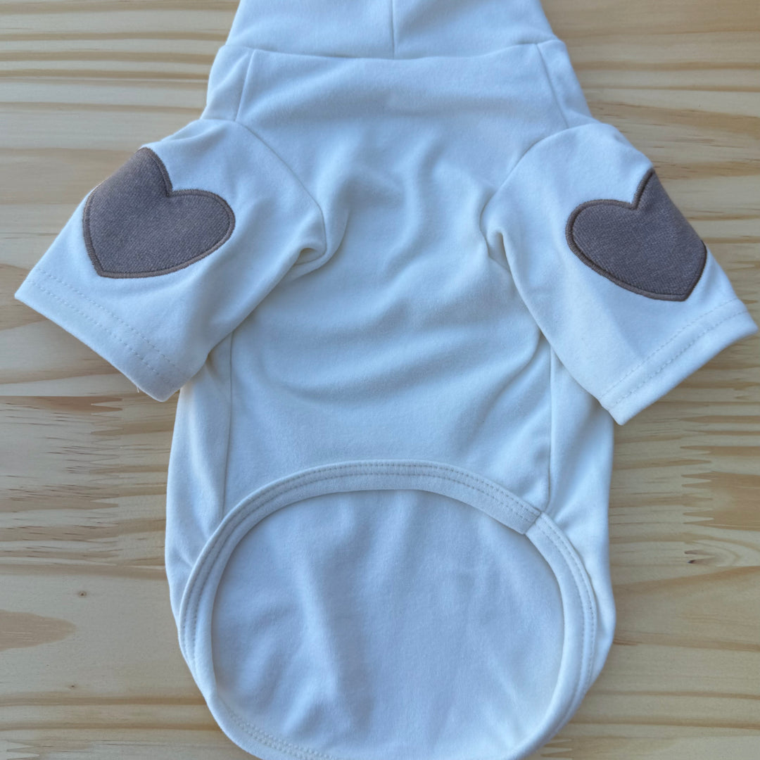 Beige dog sweater with heart-shaped arm patches on a wooden surface