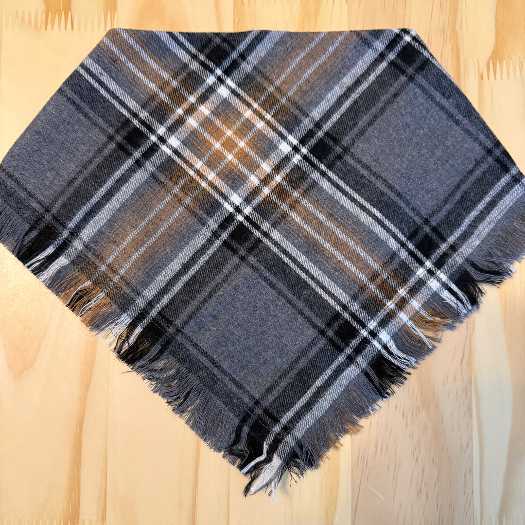 A multicolor plaid dog bandana laid flat on a light wood background.