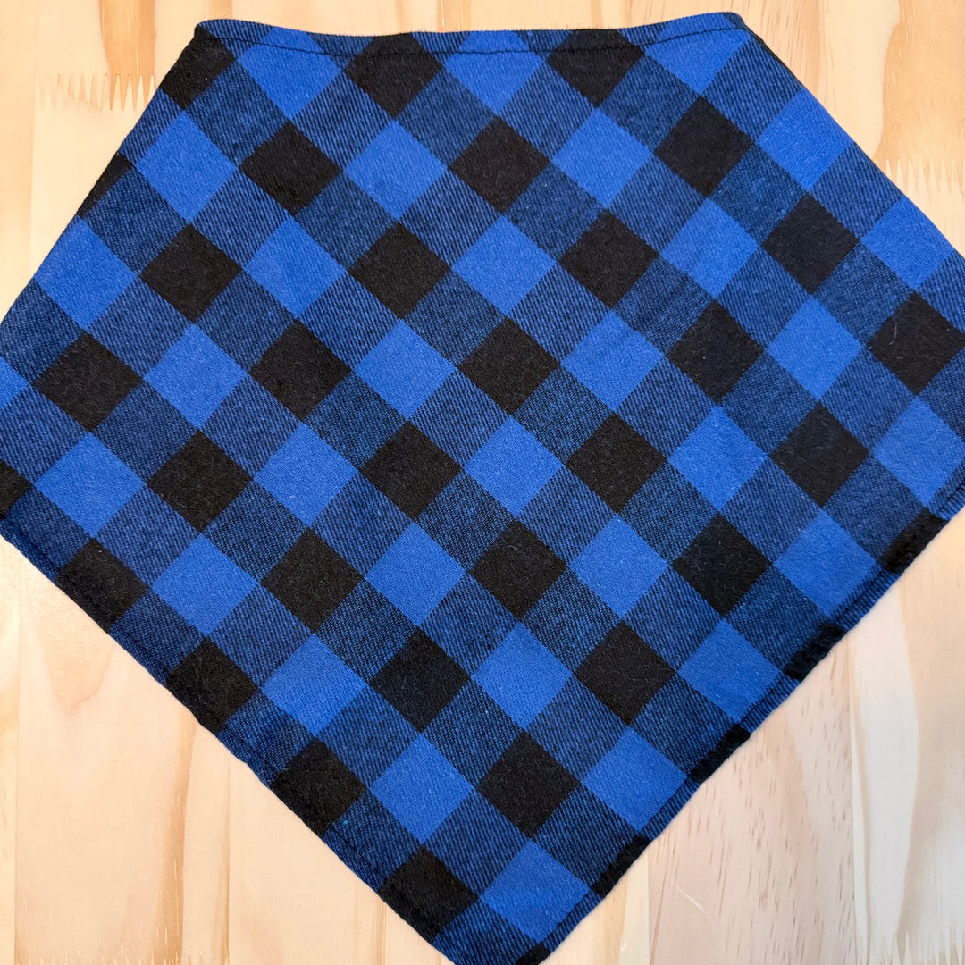 A blue and black plaid dog bandana laid flat on a light wood background.