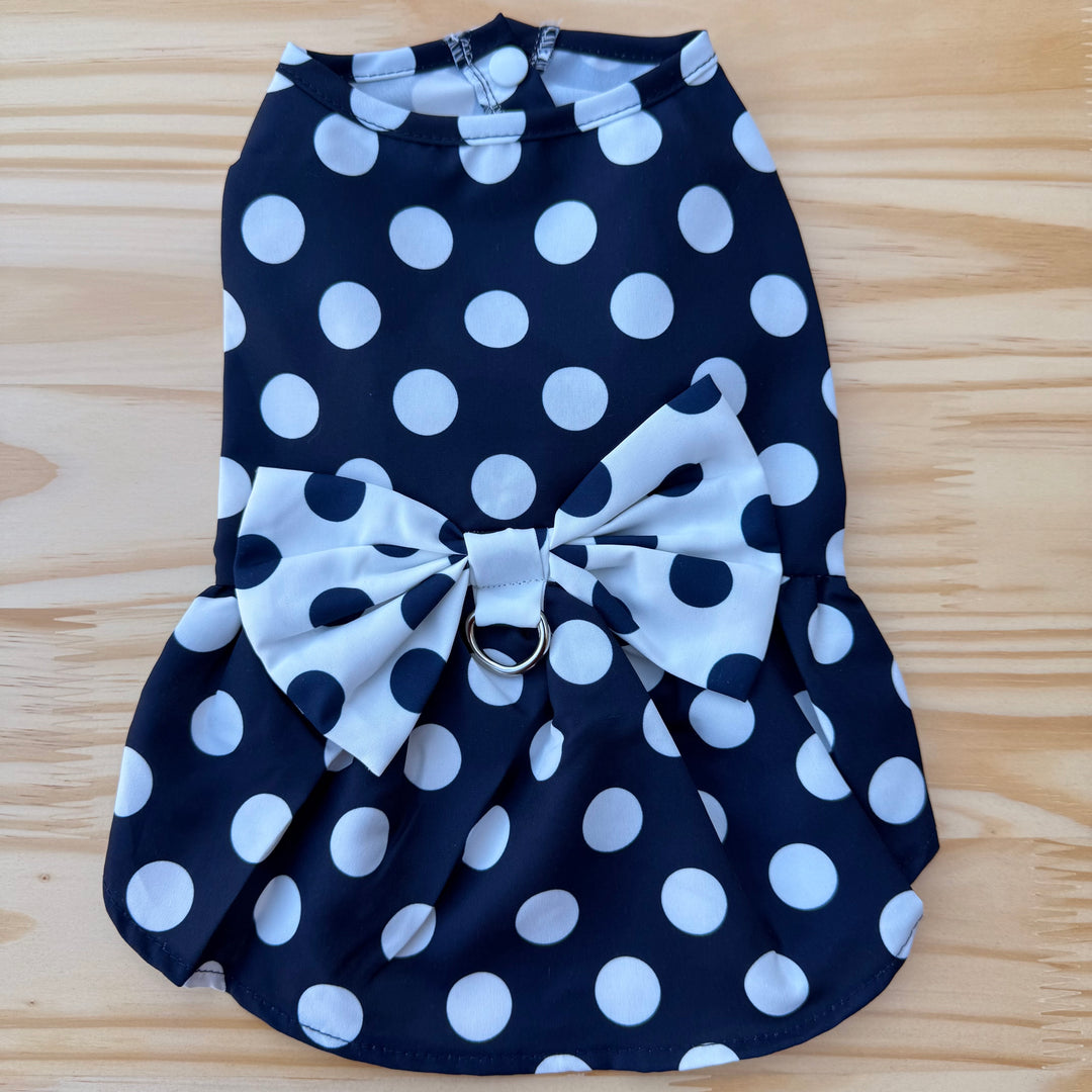 Navy blue dog dress with white polka dots and a large bow on a wooden surface