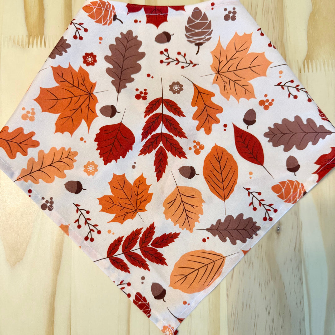 A fall leaves dog bandana laid flat on a light wood background.