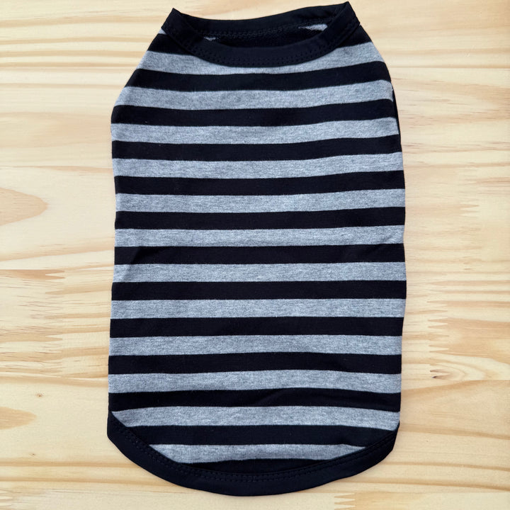 Striped dog shirt with black and gray horizontal stripes on a wooden surface