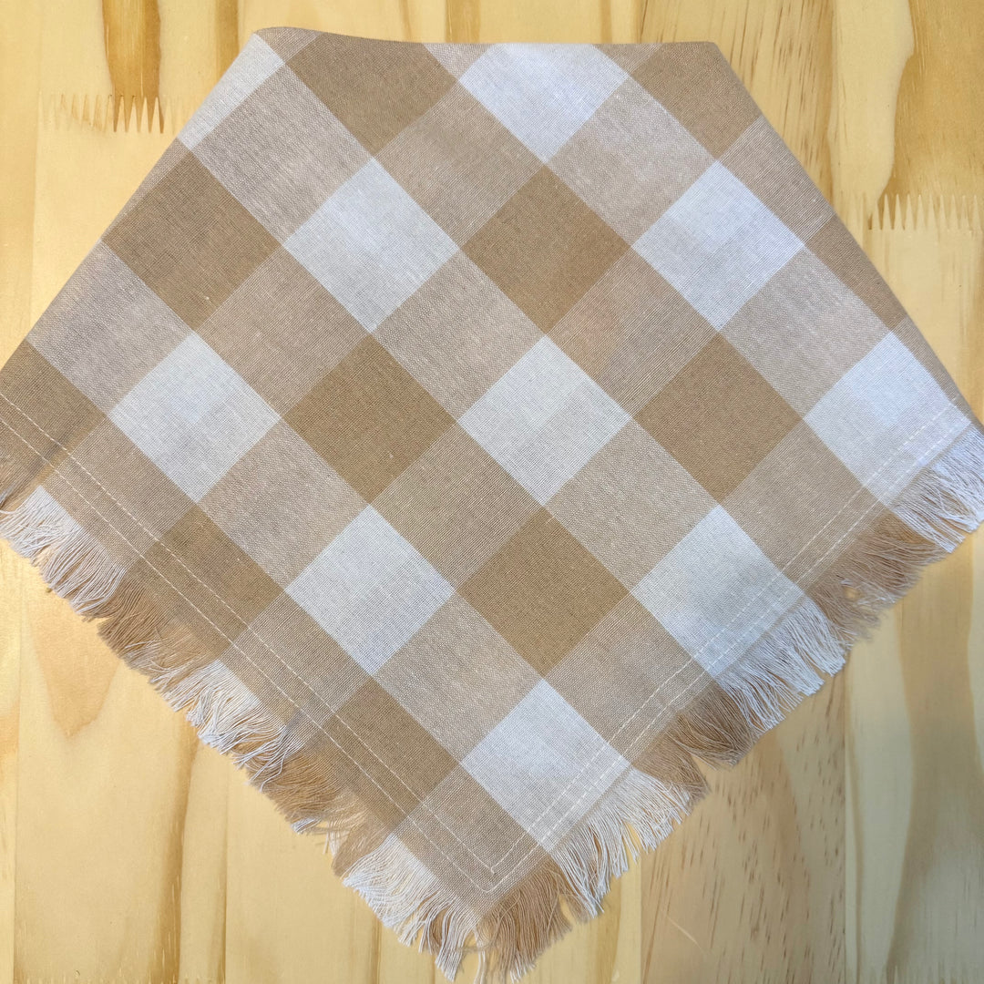 A khaki and white plaid dog bandana laid flat on a light wood background.