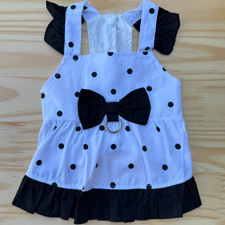 White dog dress with black polka dots and a large black bow on a wooden surface