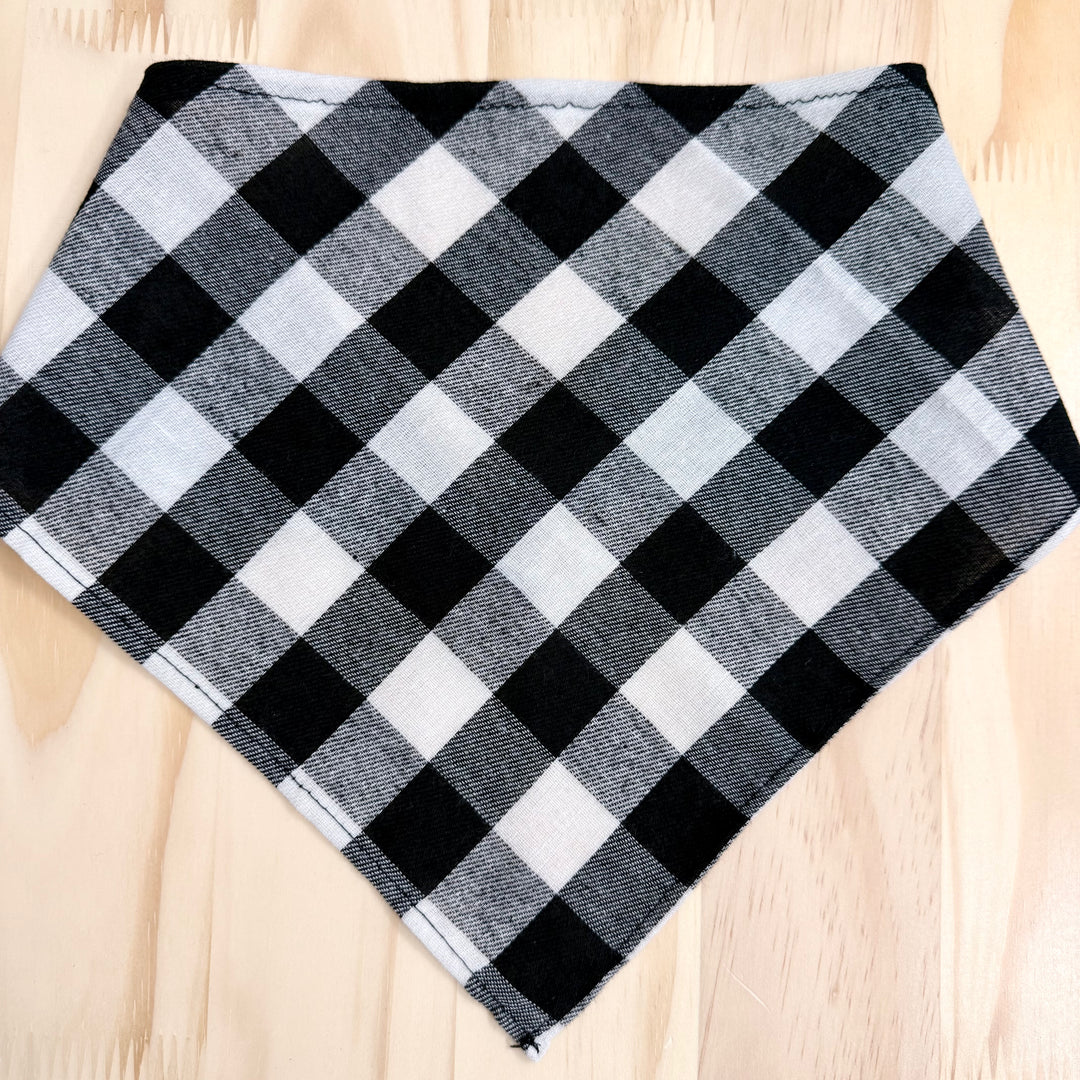 A black and white plaid dog bandana laid flat on a light wood background.